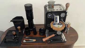 A black Geimori GU63 coffee grinder placed on a countertop next to an espresso machine.
