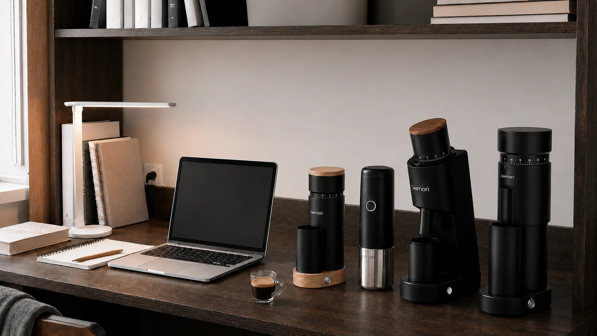 A set of black Mennip coffee brewing and grinding devices arranged on a wooden desk in a home office setting, alongside a laptop, lamp, and espresso cup.slider_item_QDe6nh